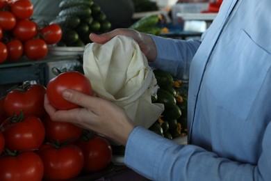 Woman putting tomato into cotton eco bag at wholesale market, closeup. Life without plastic