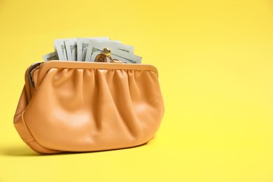 Stylish beige leather purse with dollar banknotes on yellow background. Space for text