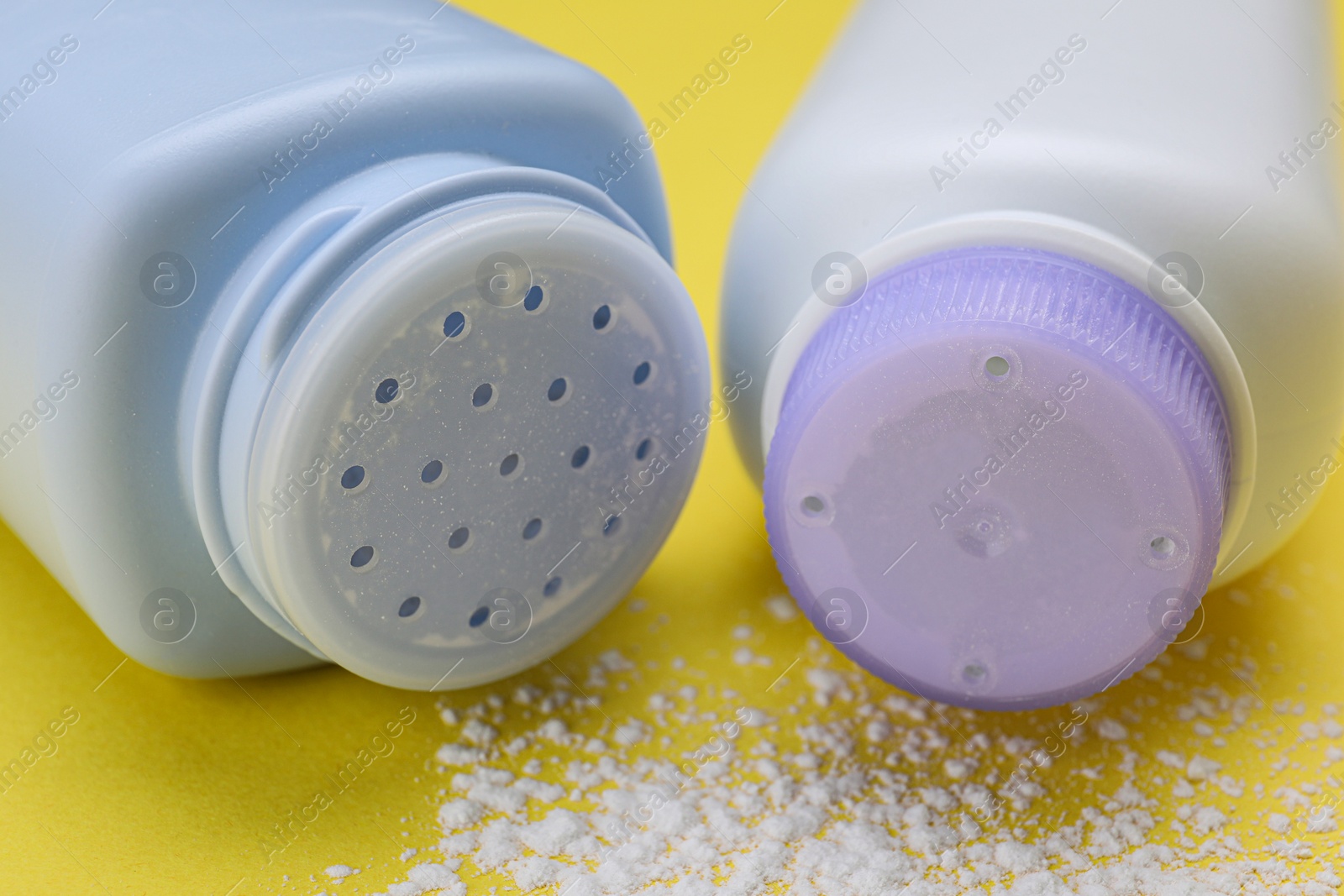 Photo of Bottles and scattered dusting powder on yellow background, closeup. Baby cosmetic products