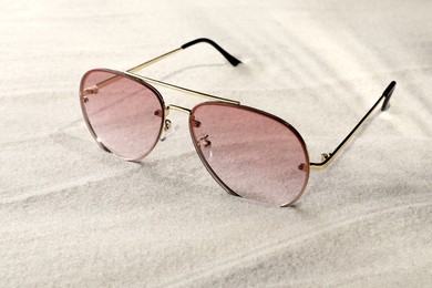 Photo of New stylish sunglasses on sand. Fashionable accessory