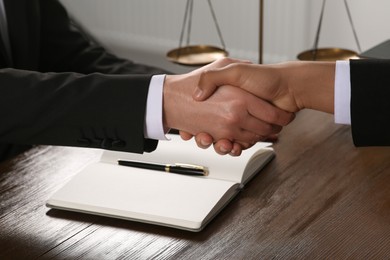 Photo of Law and justice. Notary with client shaking hands at wooden table, closeup