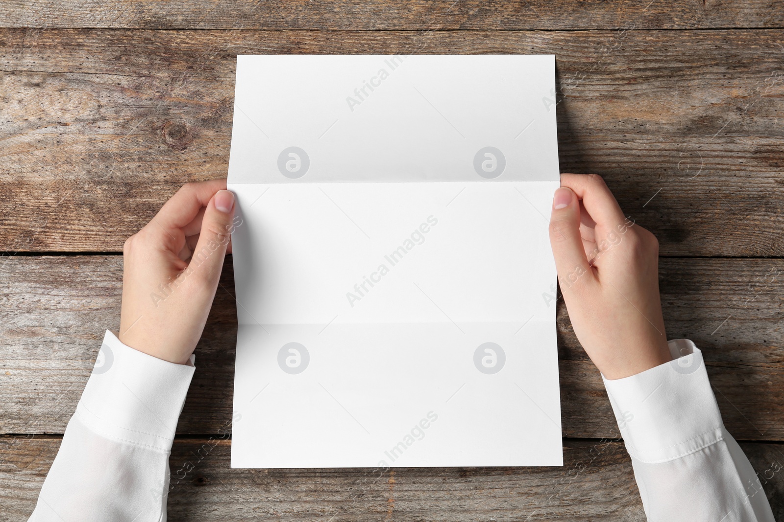 Photo of Woman holding blank brochure mock up on wooden table, top view