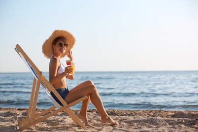 Photo of Young woman with cocktail in beach chair at seacoast. Space for text