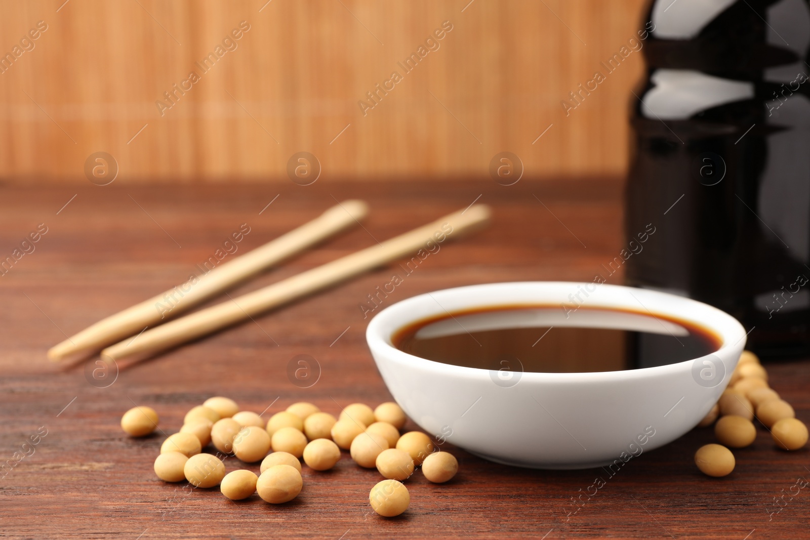 Photo of Soy sauce in bowl and soybeans on wooden table