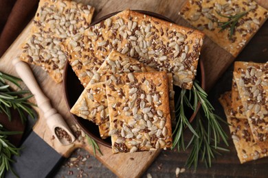 Photo of Cereal crackers with flax, sunflower, sesame seeds and rosemary on wooden table, top view