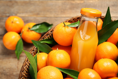 Photo of Basket with fresh tangerines and bottle of juice on wooden table, closeup