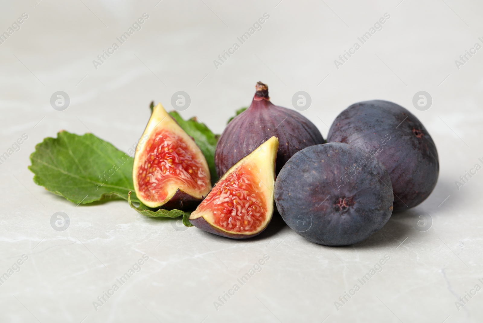 Photo of Tasty raw figs and green leaf on light grey marble table, closeup