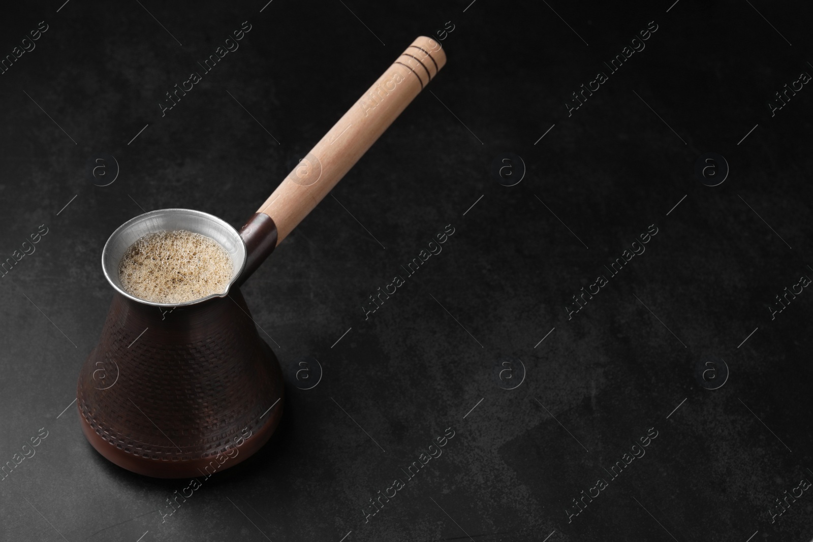 Photo of Turkish coffee in cezve on dark table, space for text