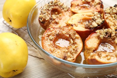 Delicious baked quinces with nuts in bowl and fresh fruits on wooden table, closeup