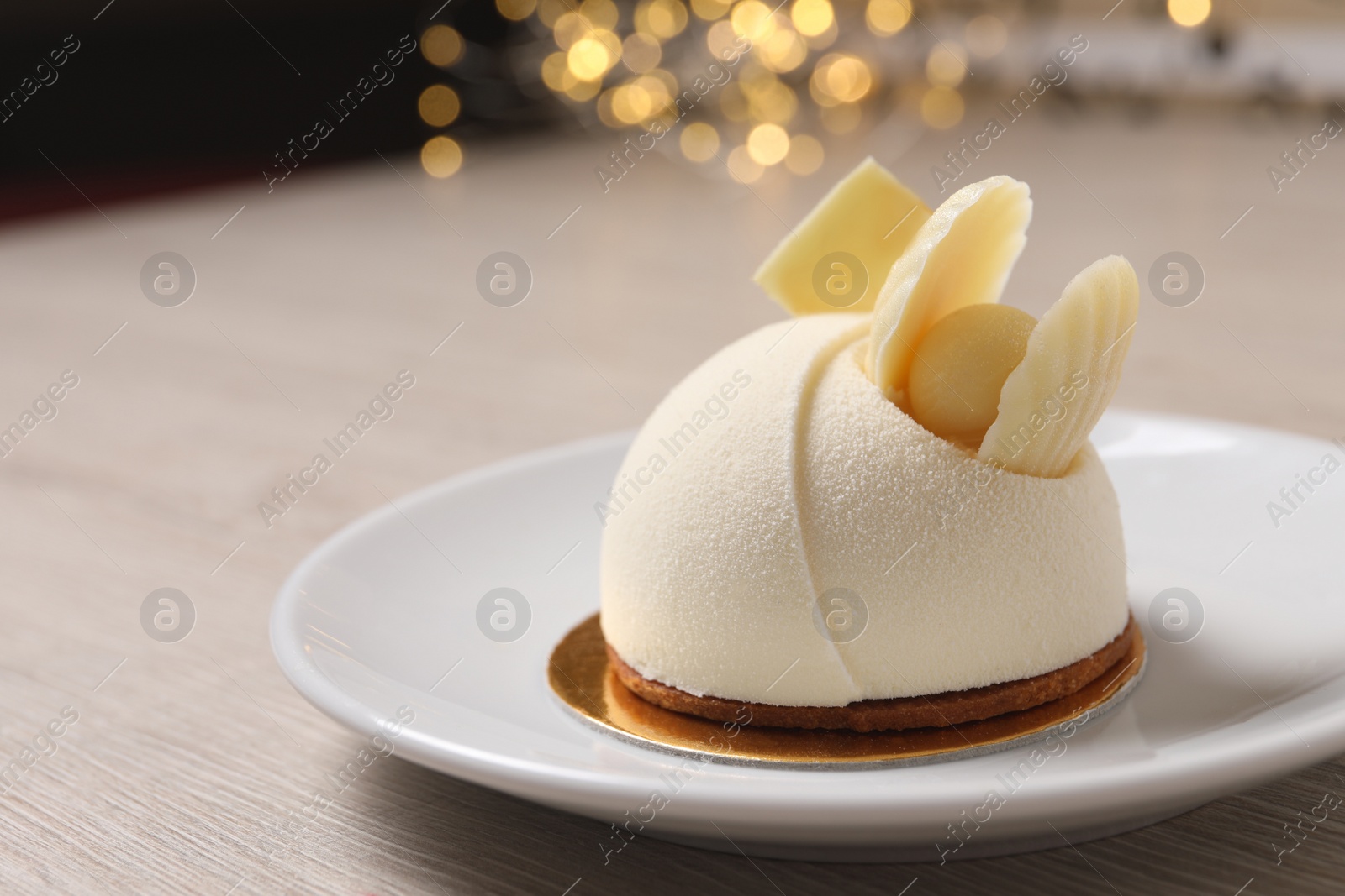 Photo of Delicious mousse cake with white chocolate on wooden table against blurred lights, closeup. Space for text