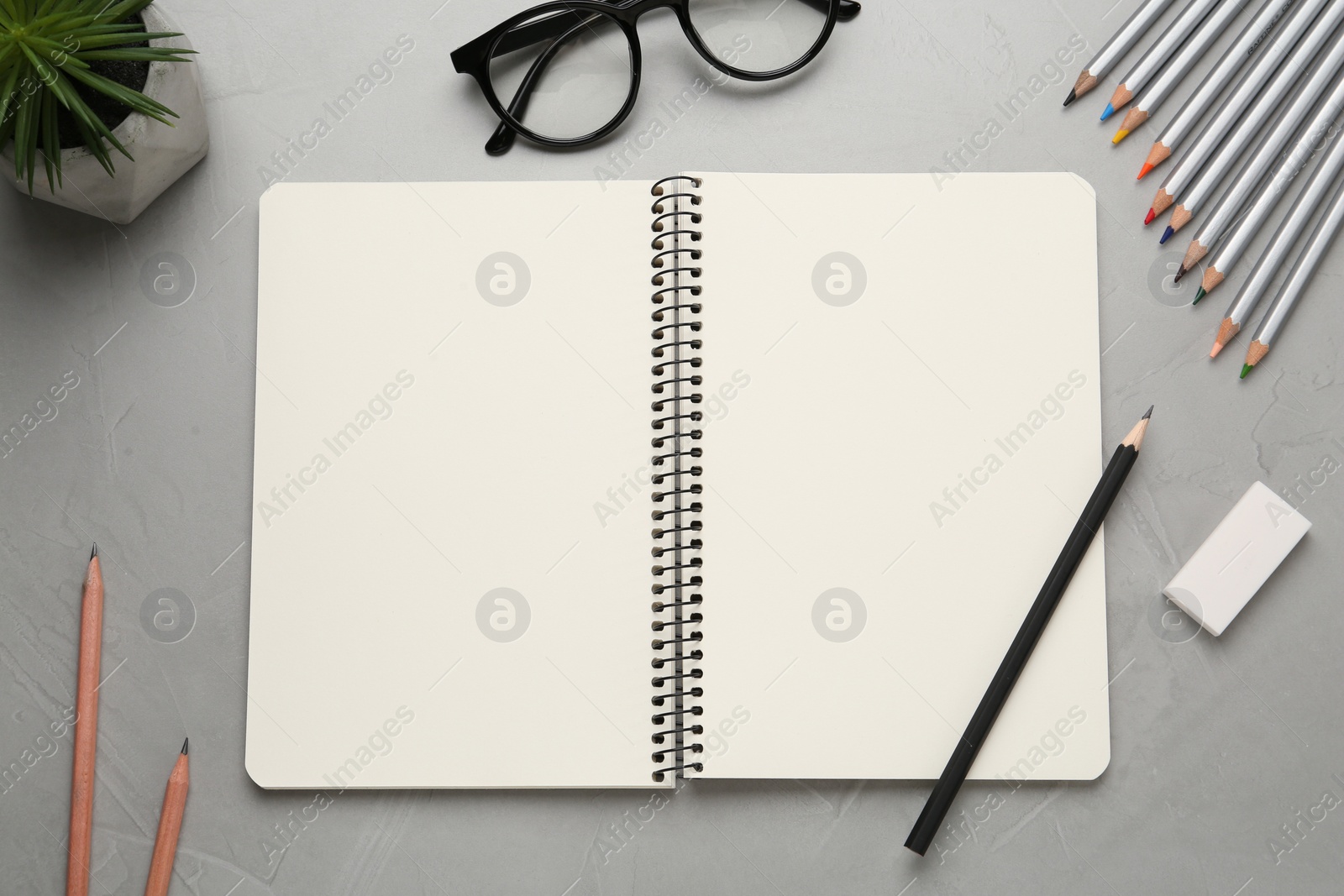 Photo of Flat lay composition with blank sketchbook on light grey stone table. Space for text