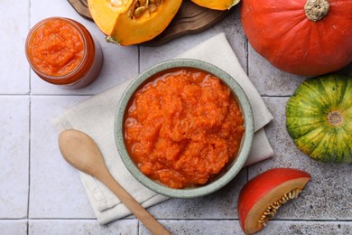 Photo of Bowl of delicious pumpkin jam and fresh pumpkins on tiled surface, flat lay