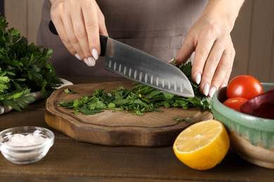 Photo of Woman cutting fresh parsley at wooden table, closeup