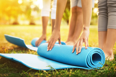 People rolling up yoga mats in park on sunny day, closeup