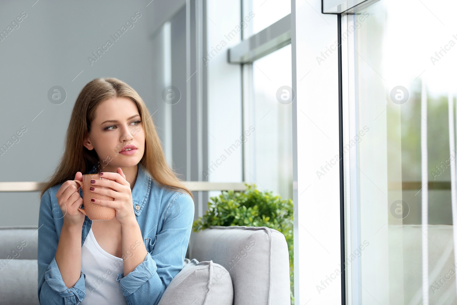 Photo of Young beautiful woman drinking morning coffee near window at home