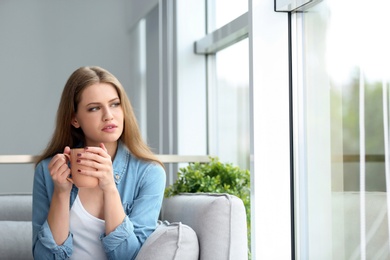 Photo of Young beautiful woman drinking morning coffee near window at home