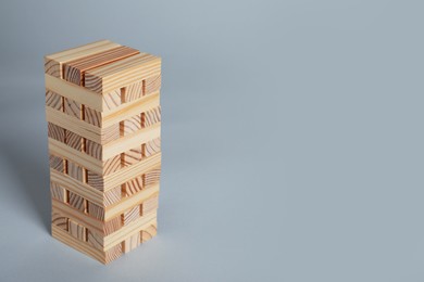Photo of Jenga tower made of wooden blocks on grey background, space for text