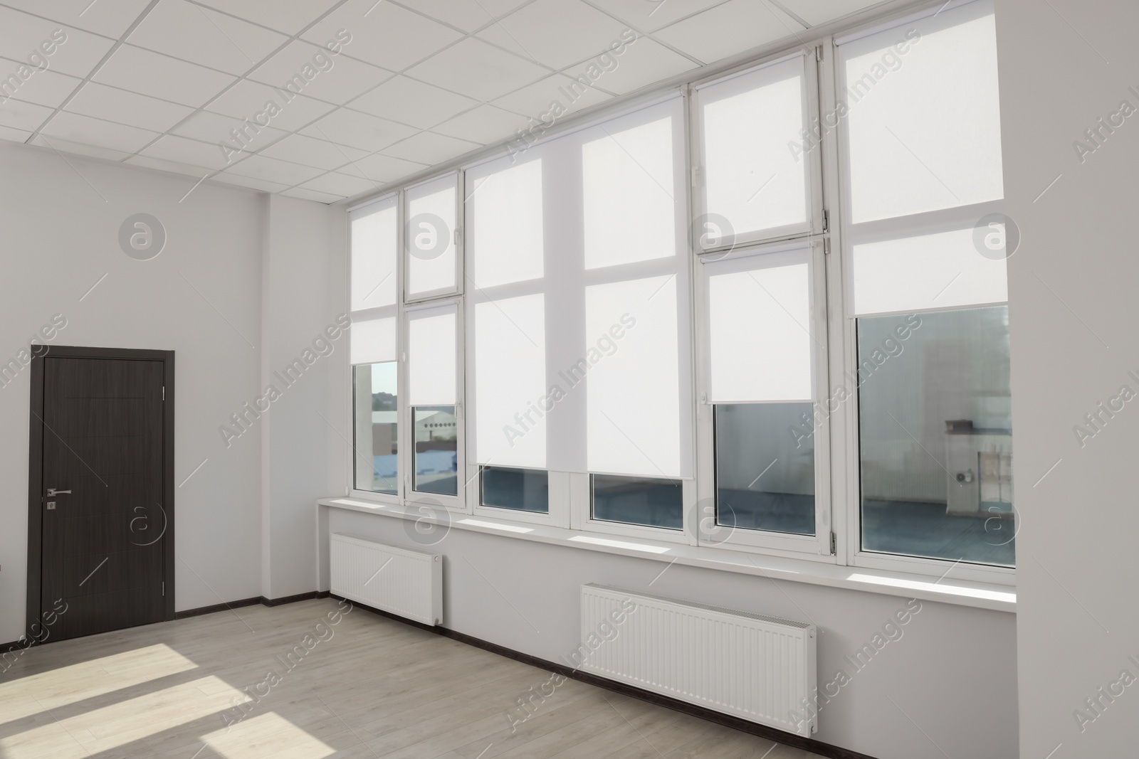 Photo of Large window with white roller blinds indoors