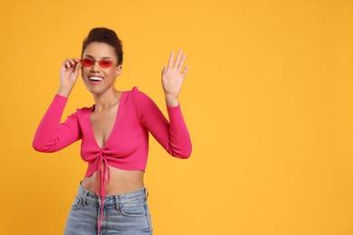 Photo of Happy young woman in stylish sunglasses dancing on orange background. Space for text