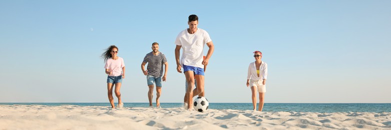 Group of friends playing football on sandy beach, low angle view. Banner design