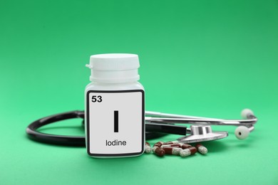 Photo of Jar with iodine pills and stethoscope on green background
