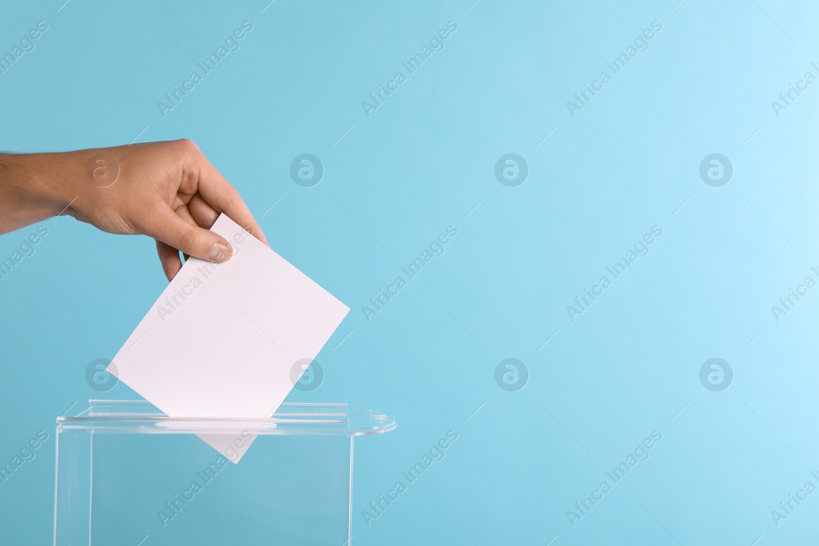 Photo of Man putting his vote into ballot box on light blue background, closeup. Space for text