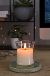 Photo of Burning candle in glass holder on wooden table indoors