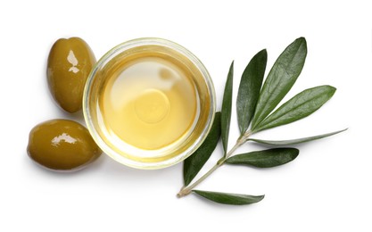 Photo of Cooking oil in bowl, olives and leaves on white background, top view