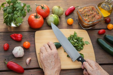 Woman cutting pepper for salsa sauce at wooden table, view from above