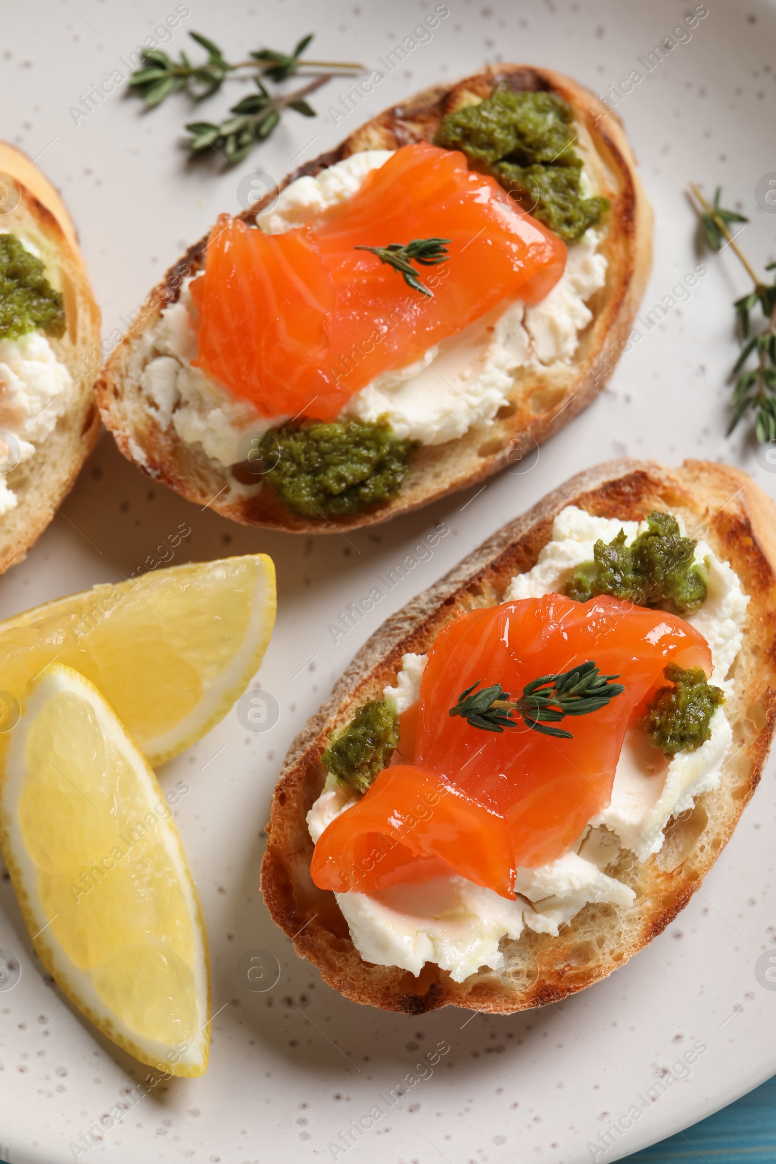 Photo of Delicious bruschettas with cream cheese, salmon and pesto sauce on plate, closeup