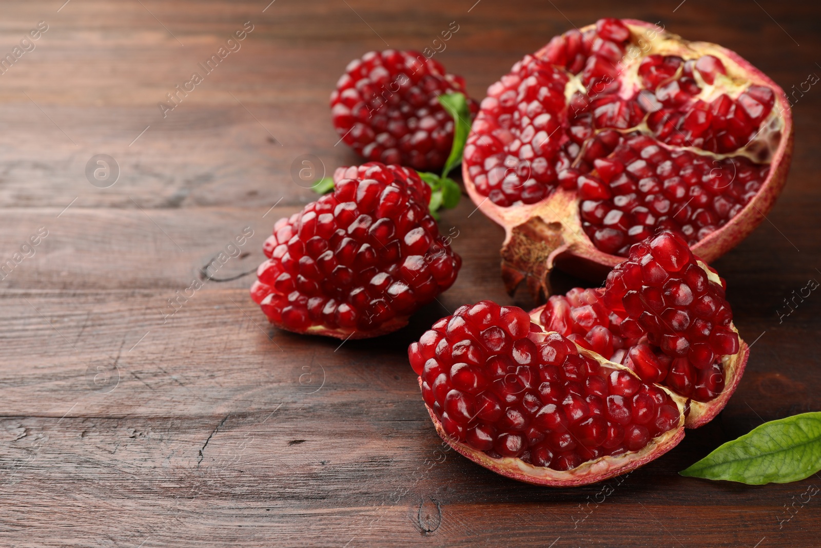 Photo of Cut fresh pomegranate and green leaves on wooden table, closeup. Space for text