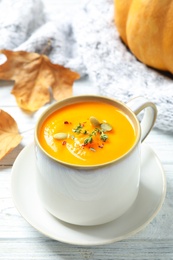 Delicious pumpkin soup in cup on white wooden table