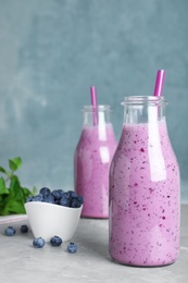 Photo of Glass bottles of blueberry smoothie and bowl with fresh berries on grey marble table