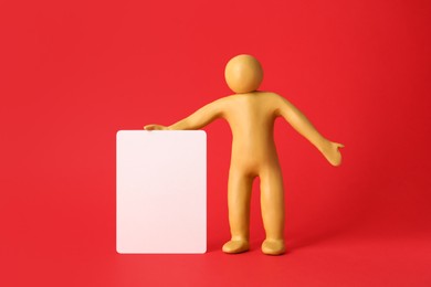 Photo of Human figure made of yellow plasticine holding blank sign on red background