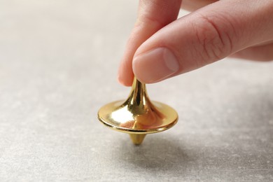 Woman playing with metal spinning top at grey textured background, closeup