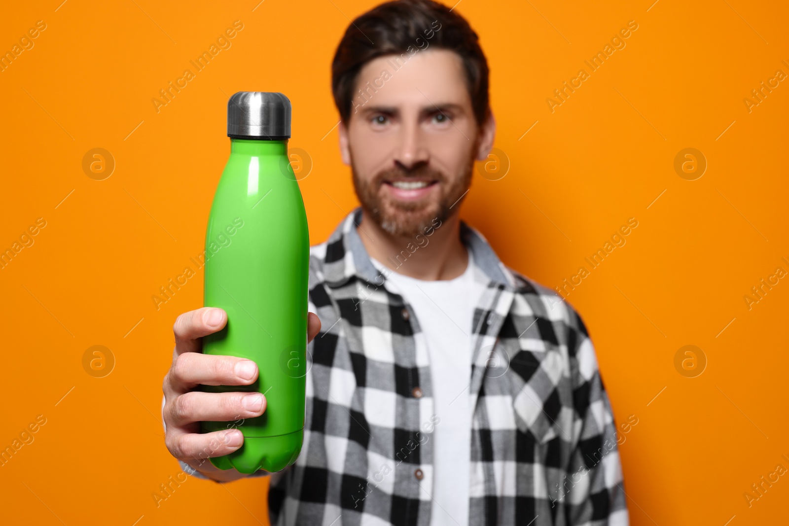 Photo of Man with green thermo bottle against orange background. Focus on hand