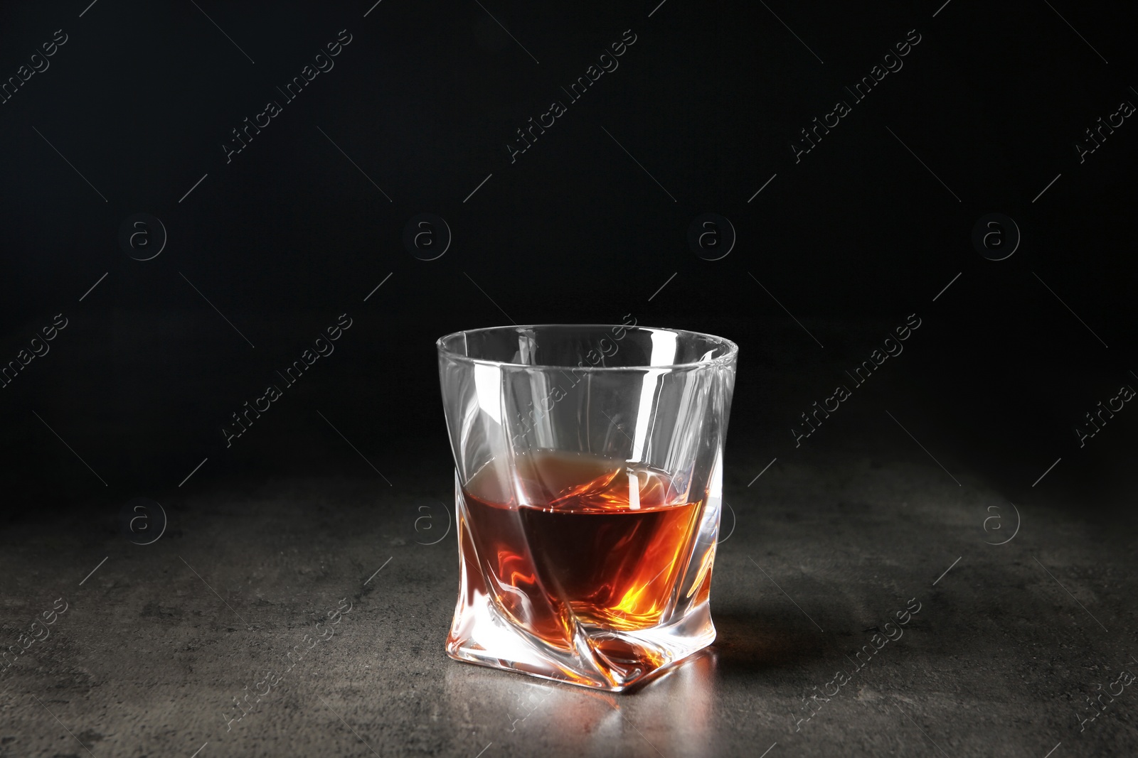 Photo of Glass of whiskey on table against dark background