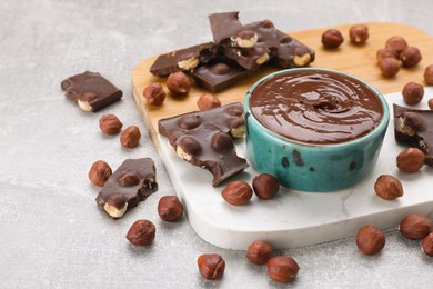 Photo of Bowl with tasty paste, chocolate pieces and nuts on wooden board, closeup