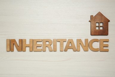 Photo of Word Inheritance made with letters and house model on wooden background, flat lay
