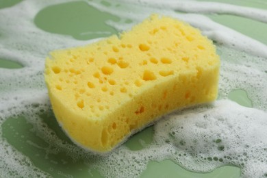 Photo of Yellow sponge with foam on green background, closeup