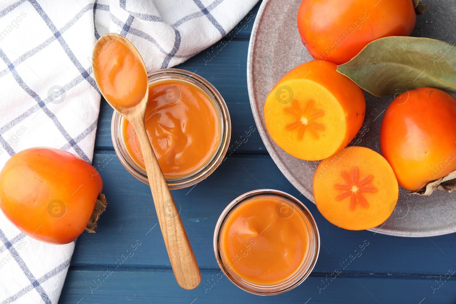 Photo of Delicious persimmon jam in glass jars served on blue wooden table, flat lay