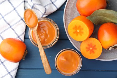 Delicious persimmon jam in glass jars served on blue wooden table, flat lay