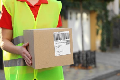 Courier in uniform with parcel outdoors, closeup. Space for text
