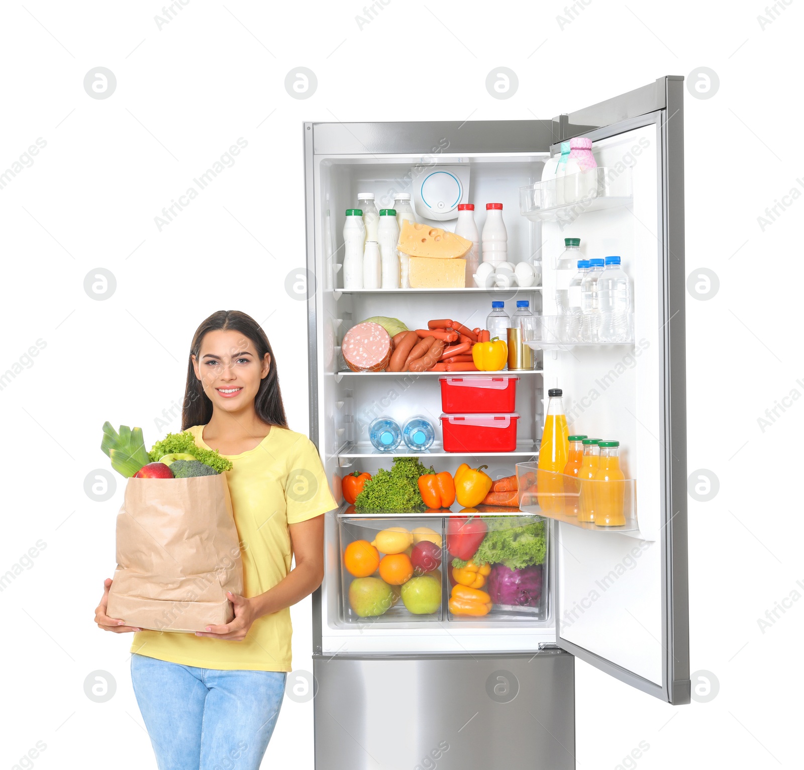 Photo of Young woman with bag of groceries near open refrigerator on white background