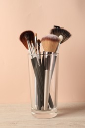 Photo of Set of professional makeup brushes on table against beige background