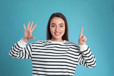 Woman showing number six with her hands on light blue background
