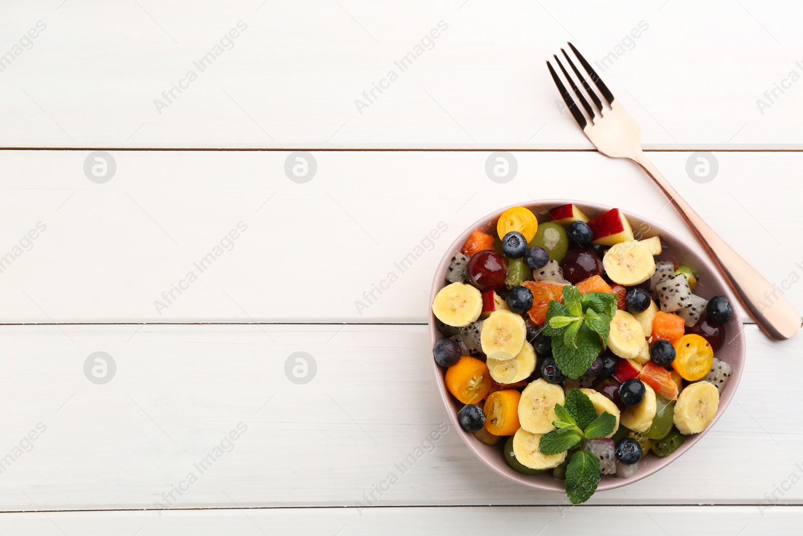 Photo of Delicious exotic fruit salad and fork on white wooden table, flat lay. Space for text
