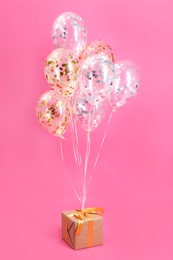 Bright balloons and gift box on color background