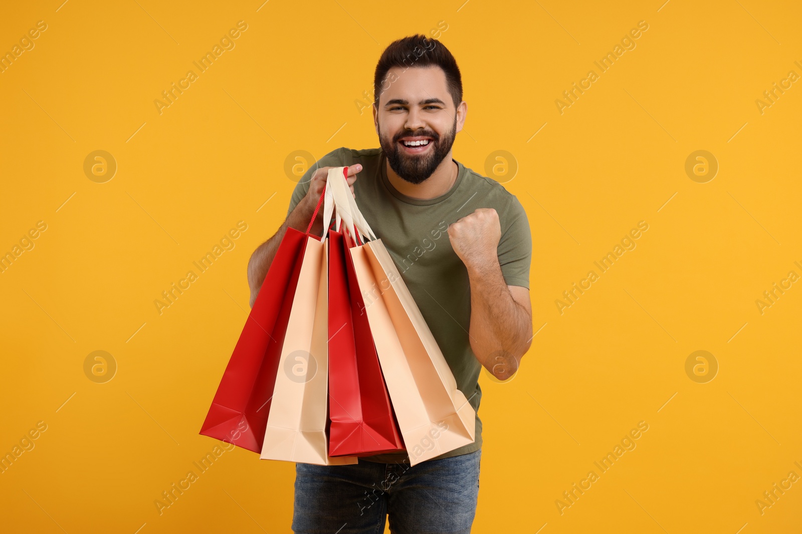 Photo of Excited man with many paper shopping bags on orange background