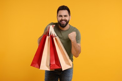Photo of Excited man with many paper shopping bags on orange background
